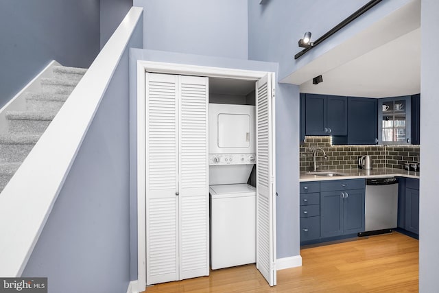 kitchen with light hardwood / wood-style flooring, tasteful backsplash, stacked washing maching and dryer, dishwasher, and sink