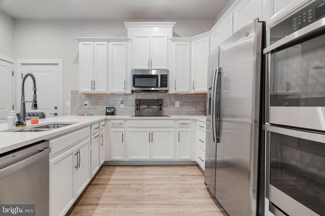 kitchen featuring backsplash, stainless steel appliances, sink, light wood-type flooring, and white cabinets