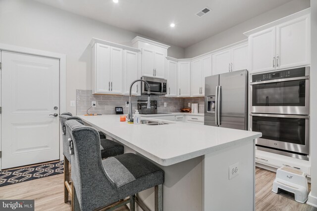 kitchen with light hardwood / wood-style floors, appliances with stainless steel finishes, a kitchen breakfast bar, and backsplash