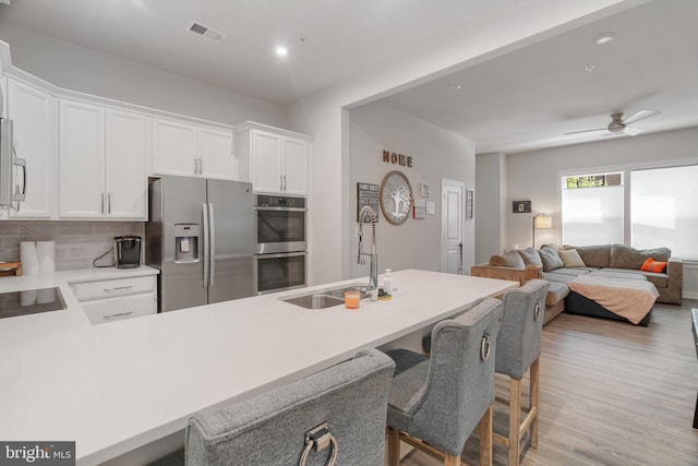 kitchen with light wood-type flooring, tasteful backsplash, white cabinetry, appliances with stainless steel finishes, and sink