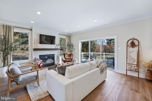 living room with a wealth of natural light, ornamental molding, a tiled fireplace, and hardwood / wood-style flooring