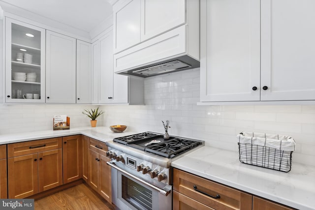 kitchen with white cabinetry, hardwood / wood-style flooring, light stone counters, and high end stainless steel range oven