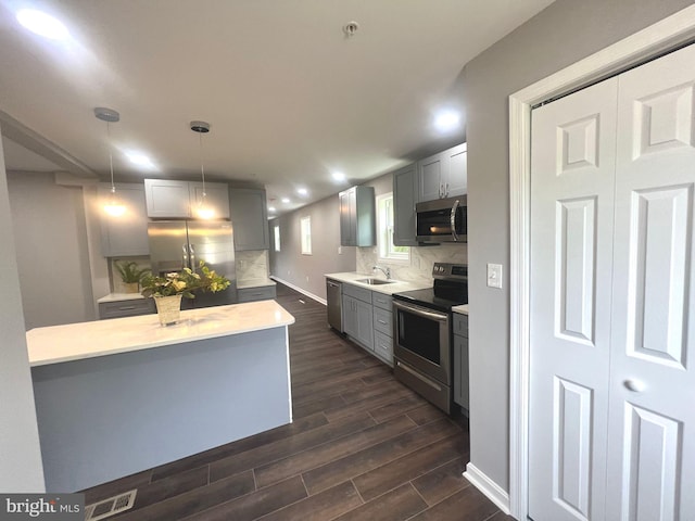 kitchen featuring stainless steel appliances, dark hardwood / wood-style flooring, pendant lighting, backsplash, and gray cabinetry