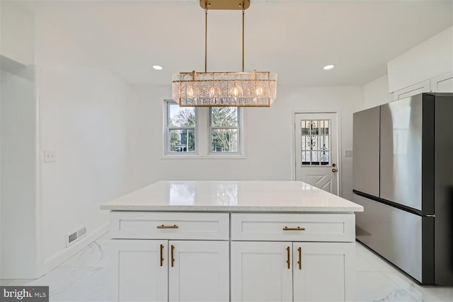 kitchen featuring decorative light fixtures, a center island, stainless steel refrigerator, light stone countertops, and white cabinets