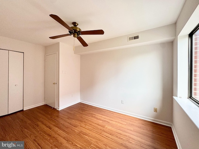 unfurnished bedroom featuring ceiling fan, multiple windows, hardwood / wood-style flooring, and a closet