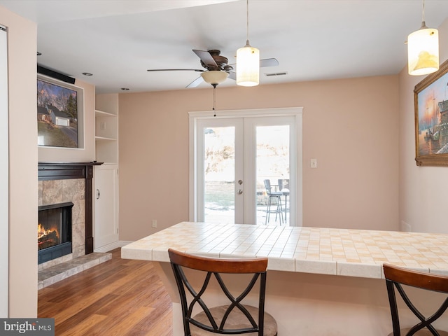 dining space with hardwood / wood-style flooring, a tile fireplace, ceiling fan, and french doors