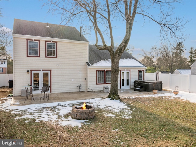 snow covered rear of property with a patio, a hot tub, french doors, and an outdoor fire pit