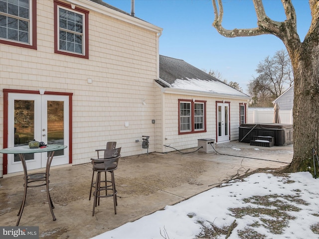 snow covered rear of property with a hot tub, a patio, and french doors