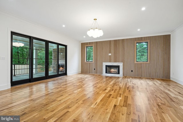 unfurnished living room featuring wood walls, light hardwood / wood-style floors, crown molding, and a chandelier