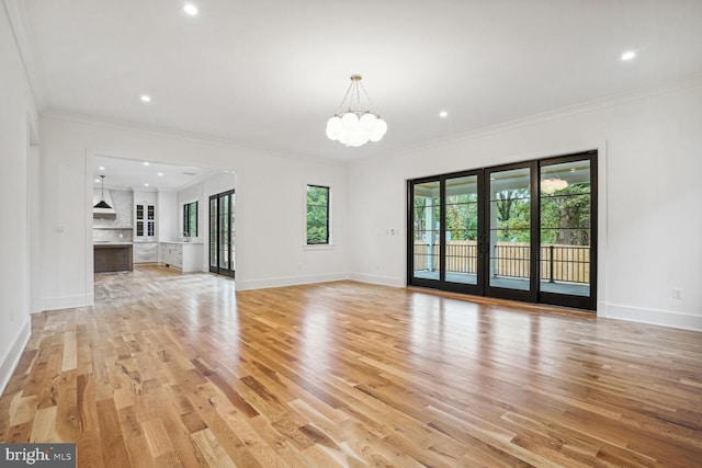 unfurnished living room featuring light hardwood / wood-style flooring, a notable chandelier, and ornamental molding