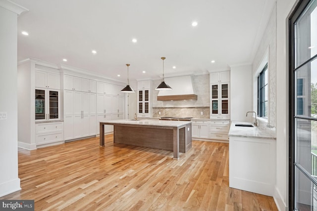 kitchen featuring white cabinetry, sink, a spacious island, pendant lighting, and custom exhaust hood