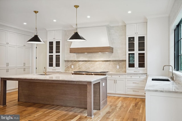 kitchen featuring light stone counters, white cabinets, decorative light fixtures, and custom range hood