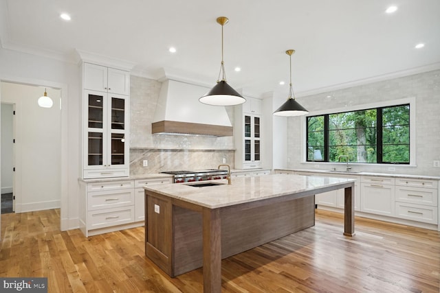 kitchen with premium range hood, white cabinetry, a kitchen island with sink, and light stone counters