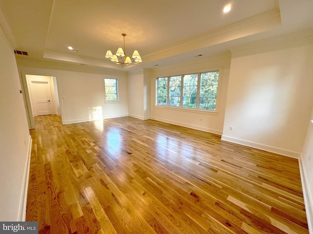 empty room with a notable chandelier, light hardwood / wood-style floors, ornamental molding, and a tray ceiling