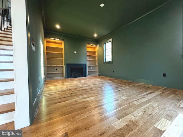 unfurnished living room with crown molding, built in features, and hardwood / wood-style floors