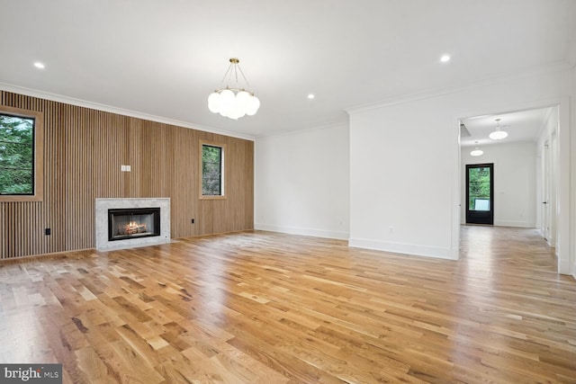 unfurnished living room featuring wooden walls, a high end fireplace, light hardwood / wood-style floors, and ornamental molding