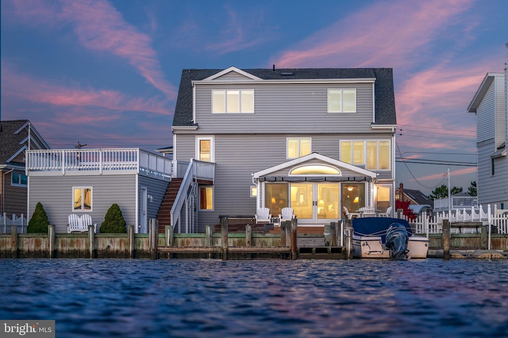 rear view of property featuring a shingled roof, a deck with water view, fence, and a hot tub