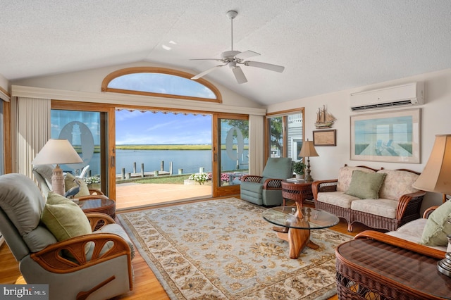 living room featuring ceiling fan, light hardwood / wood-style floors, vaulted ceiling, a water view, and a wall mounted AC