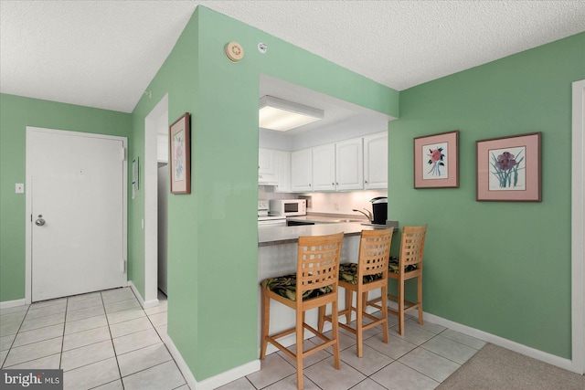 kitchen featuring a breakfast bar, a textured ceiling, light tile patterned floors, kitchen peninsula, and white cabinets