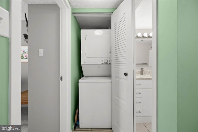 laundry area featuring light tile patterned floors, stacked washer and clothes dryer, a textured ceiling, and sink