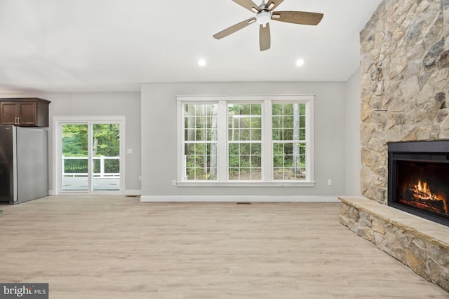 unfurnished living room featuring light hardwood / wood-style floors, a stone fireplace, and ceiling fan