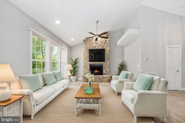 living room featuring light wood-type flooring, a fireplace, ceiling fan, and high vaulted ceiling