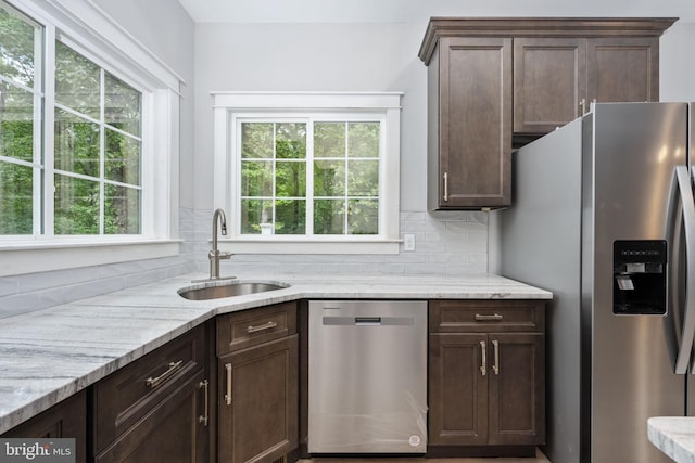 kitchen with dark brown cabinets, light stone counters, sink, decorative backsplash, and stainless steel appliances