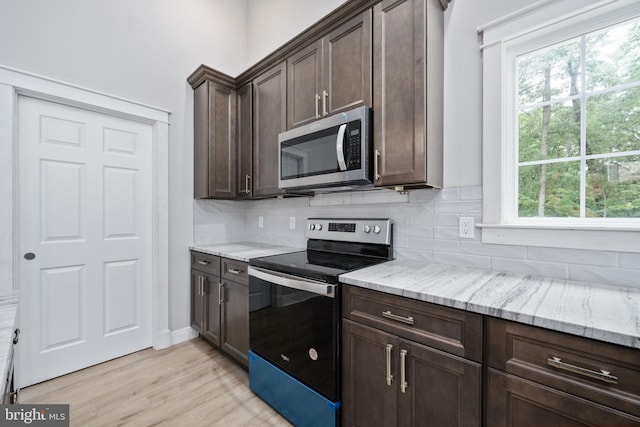 kitchen with dark brown cabinets, light stone counters, decorative backsplash, stainless steel appliances, and light hardwood / wood-style flooring