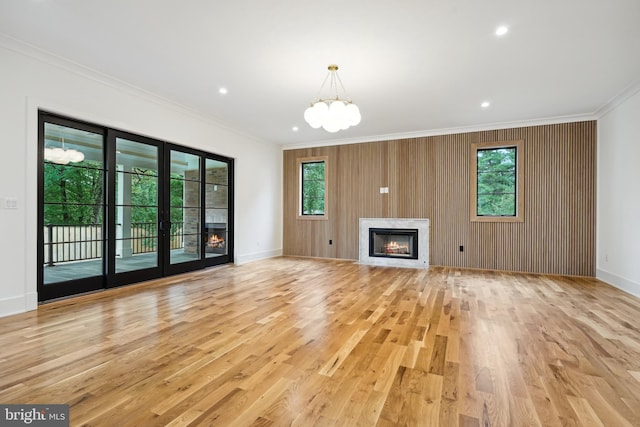 unfurnished living room featuring light wood-style floors, ornamental molding, a wealth of natural light, and a high end fireplace