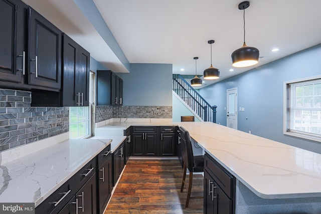 kitchen featuring tasteful backsplash, dark hardwood / wood-style flooring, light stone counters, and decorative light fixtures