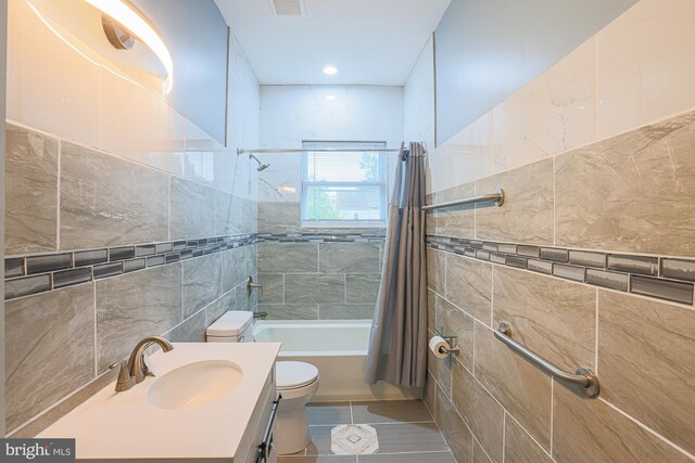 full bathroom with tile walls, shower / bath combination with curtain, toilet, tile patterned floors, and vanity