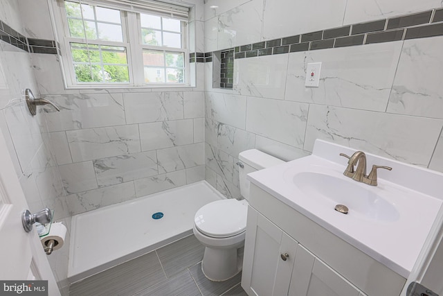 bathroom featuring toilet, tile patterned floors, tile walls, vanity, and tiled shower