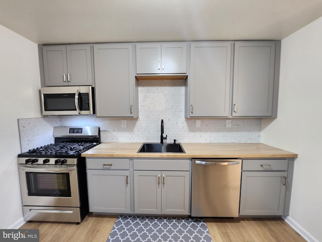 kitchen with light hardwood / wood-style floors, sink, butcher block counters, and stainless steel appliances