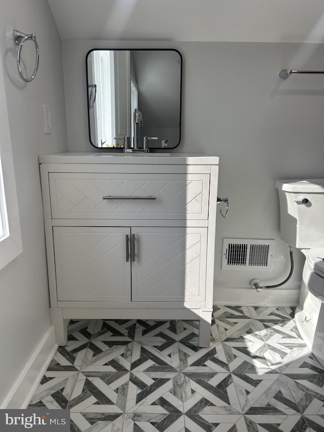 half bathroom with vanity, toilet, baseboards, and visible vents