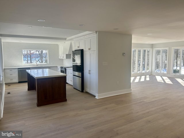 kitchen featuring a sink, open floor plan, stainless steel appliances, light wood-style floors, and wall chimney exhaust hood