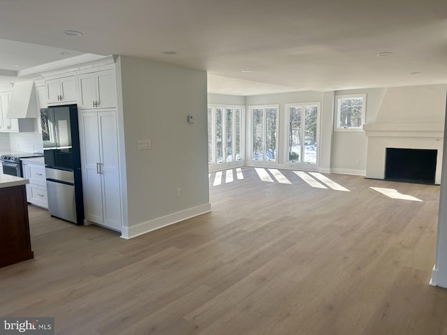 kitchen featuring light wood-style flooring, wall chimney exhaust hood, open floor plan, and stainless steel appliances