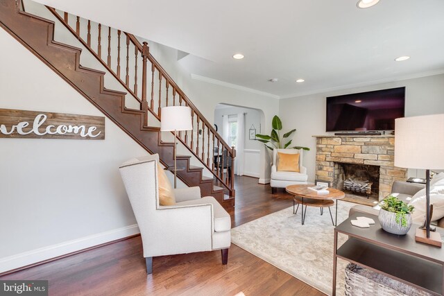 living room featuring a stone fireplace, crown molding, and dark wood-type flooring