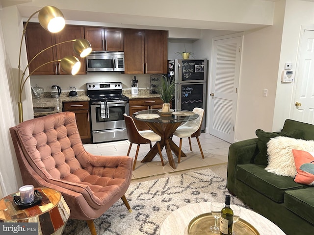 kitchen with appliances with stainless steel finishes, dark brown cabinets, light stone countertops, and light tile patterned floors