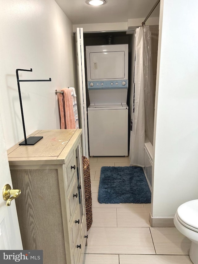 full bathroom with stacked washing maching and dryer, toilet, shower / bath combo with shower curtain, tile patterned floors, and vanity