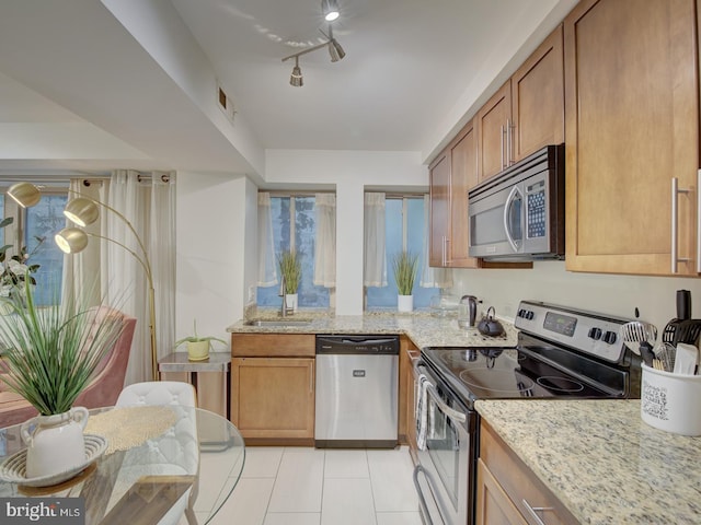 kitchen with light tile patterned flooring, rail lighting, sink, appliances with stainless steel finishes, and light stone countertops