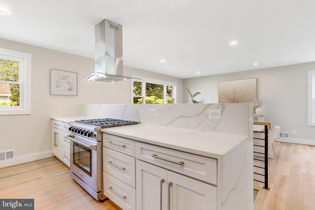 kitchen featuring light stone counters, island range hood, high end stove, white cabinets, and decorative backsplash