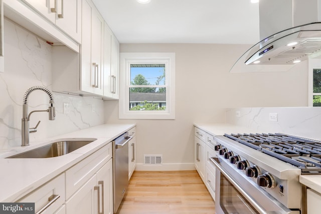 kitchen with island range hood, tasteful backsplash, white cabinetry, sink, and stainless steel appliances