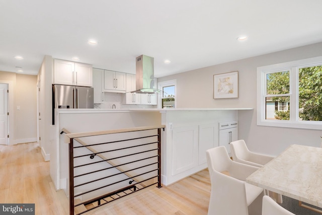 kitchen with island exhaust hood, high quality fridge, white cabinets, and light wood-type flooring