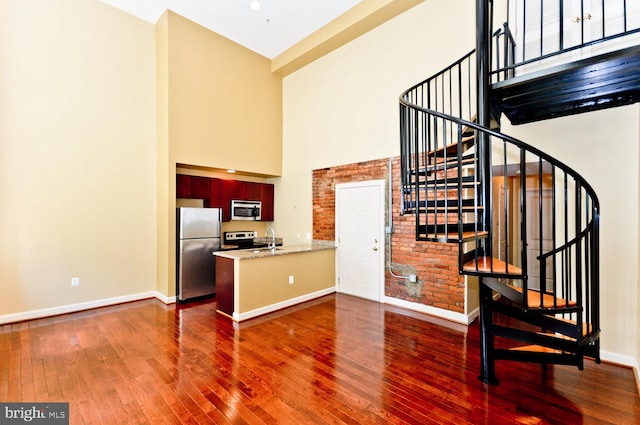 interior space featuring light stone counters, dark hardwood / wood-style floors, kitchen peninsula, a towering ceiling, and appliances with stainless steel finishes