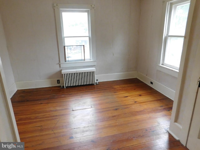 unfurnished room with radiator heating unit, a healthy amount of sunlight, and hardwood / wood-style floors