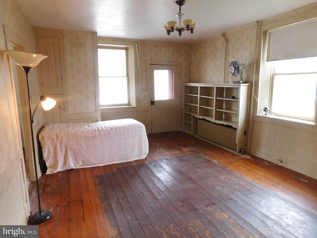 unfurnished bedroom with hardwood / wood-style flooring, radiator, and a chandelier