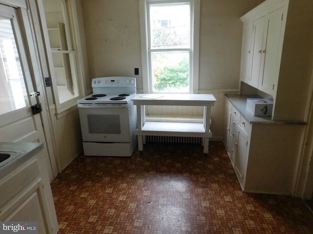 kitchen with white electric stove, dark tile patterned flooring, and white cabinets