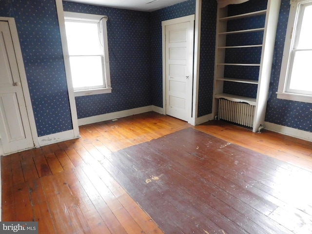 unfurnished bedroom with multiple windows, light wood-type flooring, and radiator heating unit