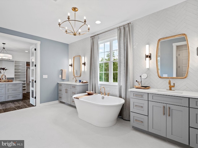 bathroom with a chandelier, vanity, a tub, tile patterned flooring, and backsplash