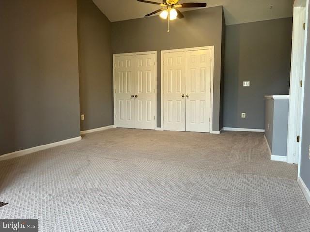 unfurnished bedroom with two closets, ceiling fan, vaulted ceiling, and carpet floors